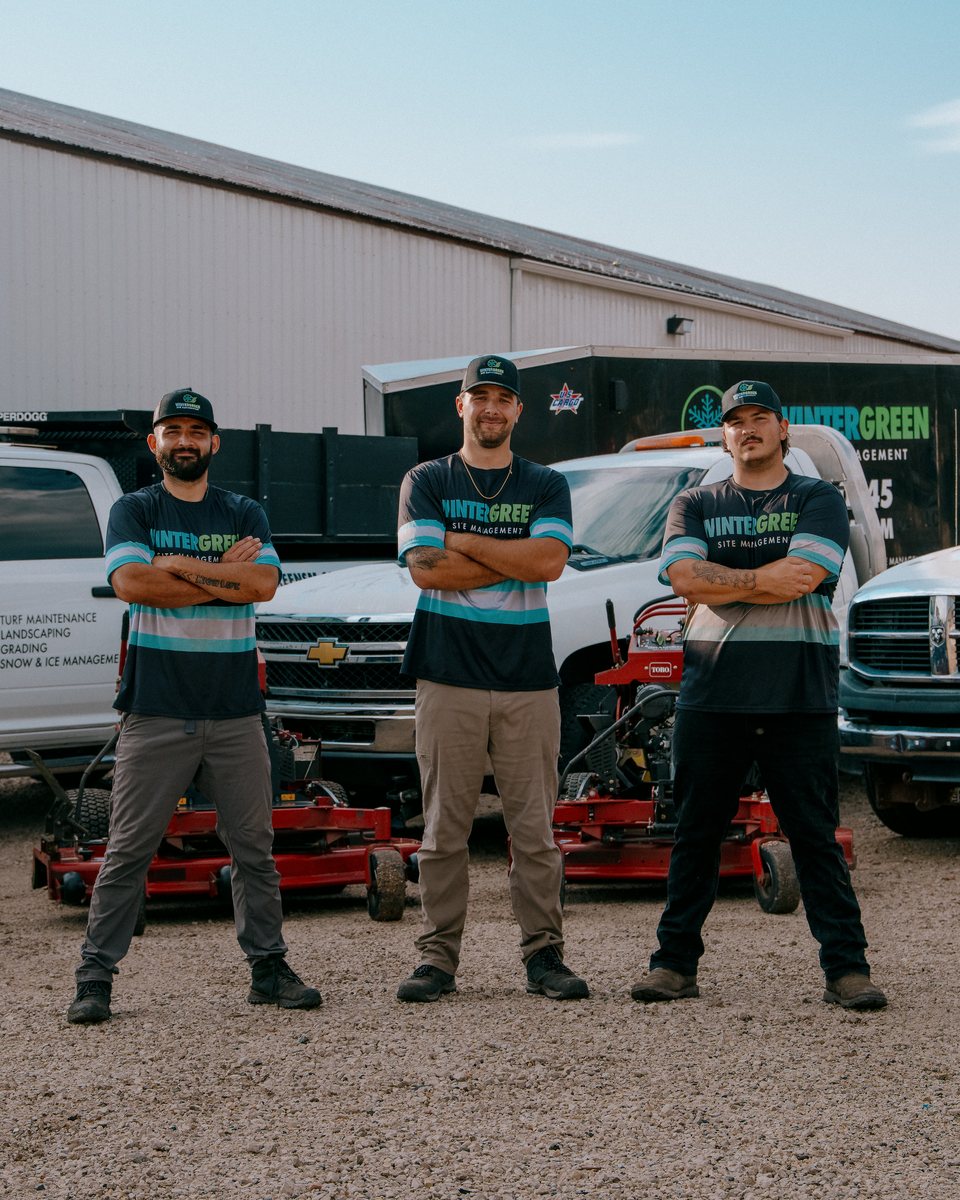 Three-person landscaping crew standing in front of their trucks and equipment
